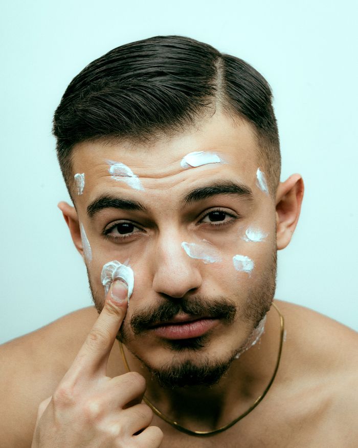 services-04 Close-up of a young man applying facial cream for skincare routine.