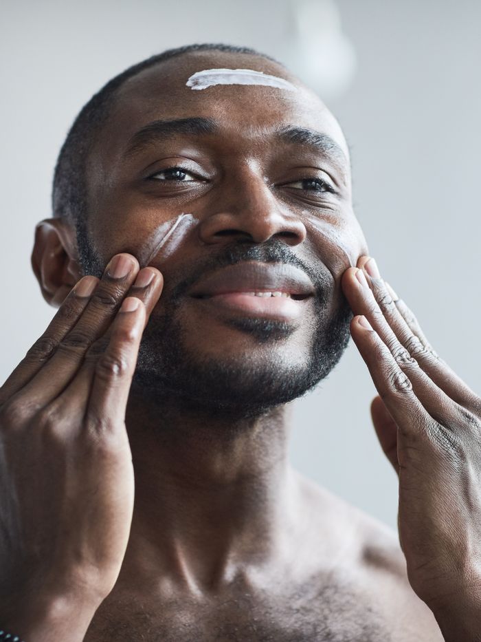 services-03 Portrait of a black man smiling while applying face cream indoors during the day.