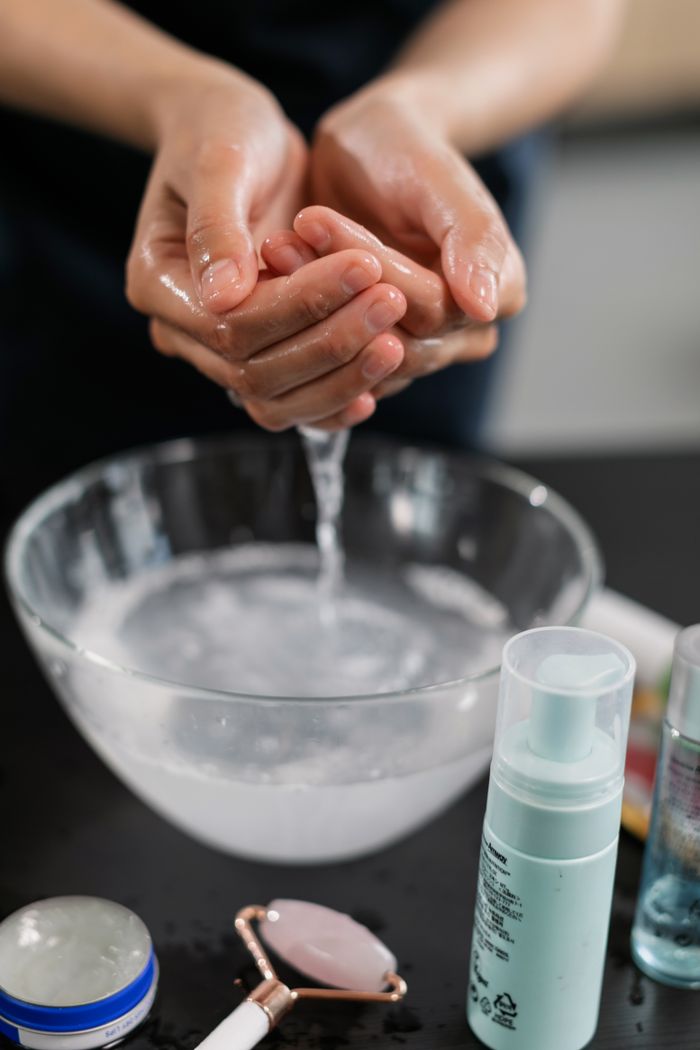 services-02 Close-up of a person washing hands, surrounded by skincare products including cosmetics and tools.