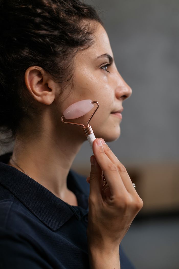 get-in-touch Side view of a woman massaging her face with a rose quartz roller in a beauty routine.